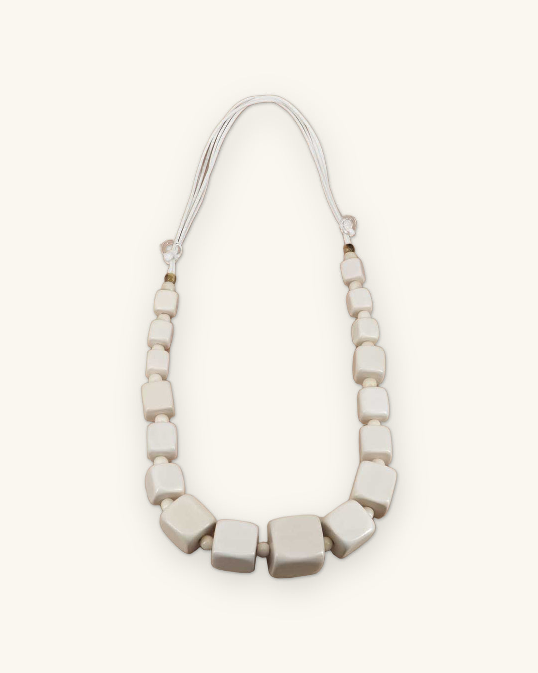Soft white graduated wood cube necklace on white cord, laid flat with small round spacer beads, shown on a sand background