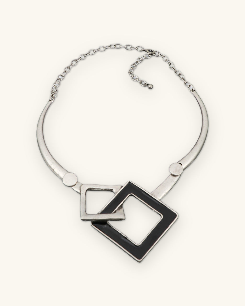 Interlocking squares collar necklace laid flat showing the rigid silver-tone collar and chain closure, shown on a sand background