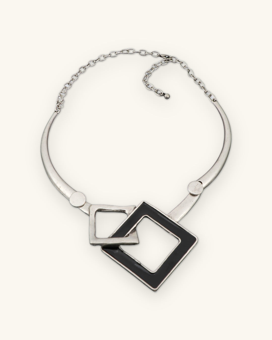 Interlocking squares collar necklace laid flat showing the rigid silver-tone collar and chain closure, shown on a sand background