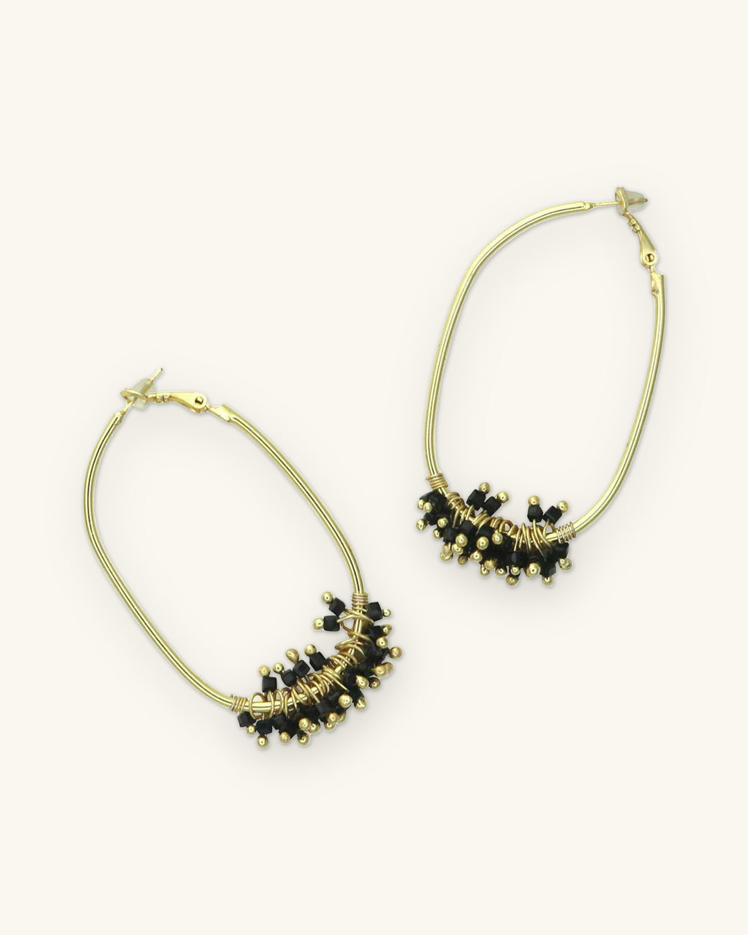 Gold-plated brass oval hoop earrings with a fringe of black glass beads, hand-wrapped in India, shown on a sand background