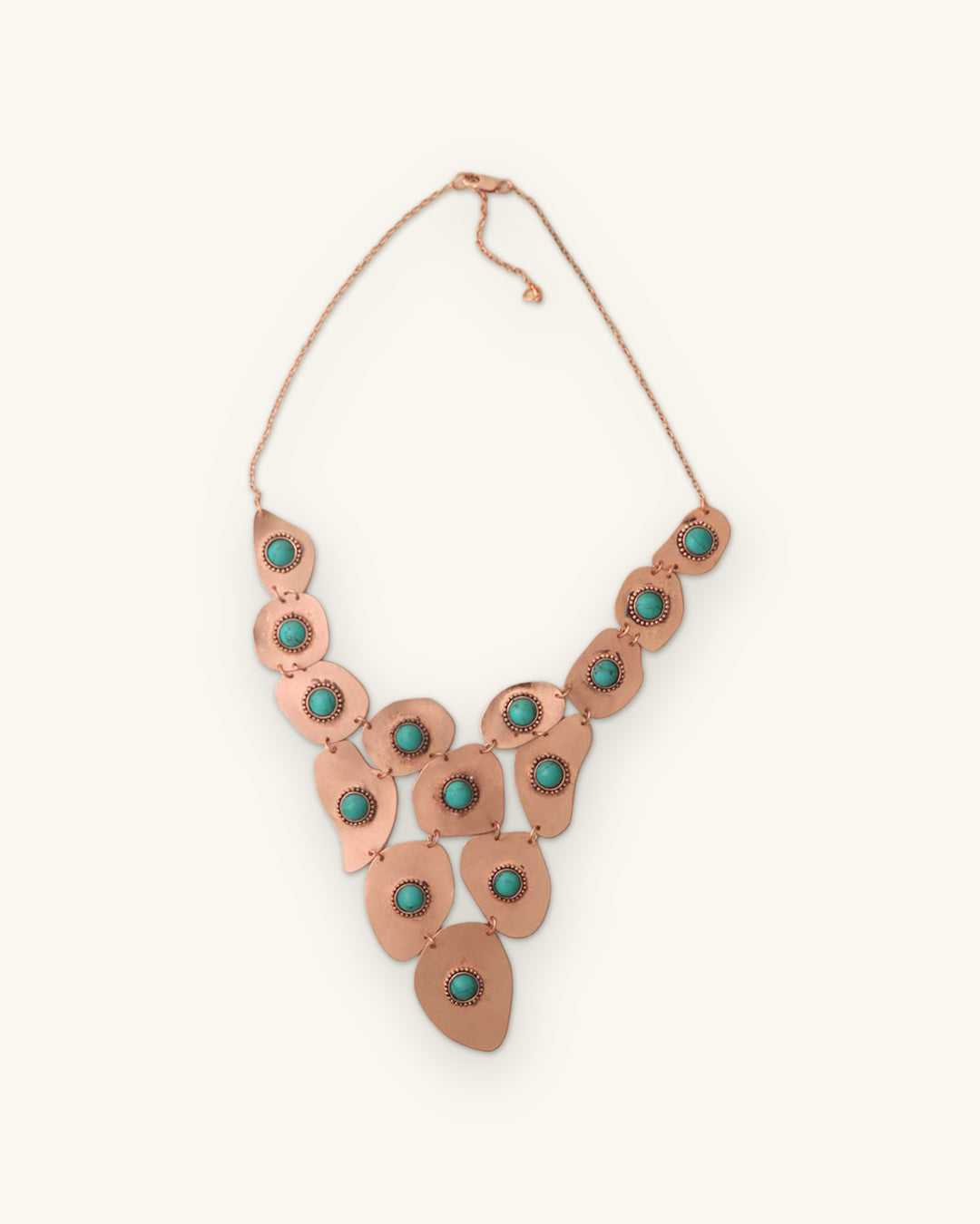 Cascading copper bib necklace of hammered plates set with turquoise-color cabochons, hand-forged in India, shown on a sand background