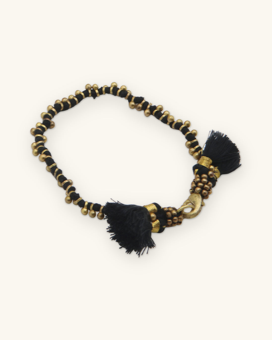 Beaded brass tassel bracelet in Black with brass lobster clasp, shown on a sand background