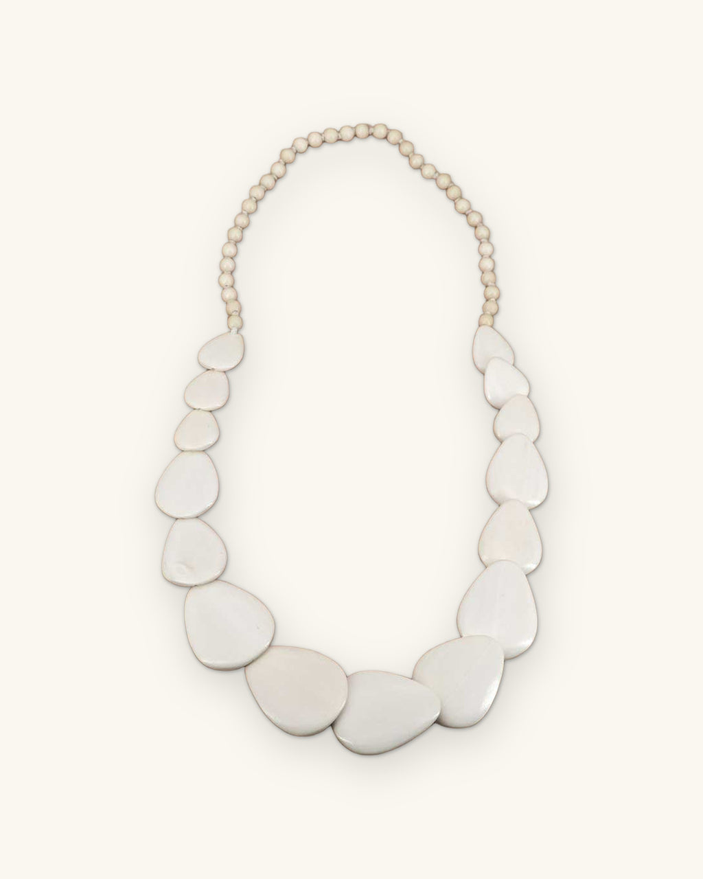 White guitar-pick shaped wood disc necklace on a round bead strand, laid flat, shown on a sand background