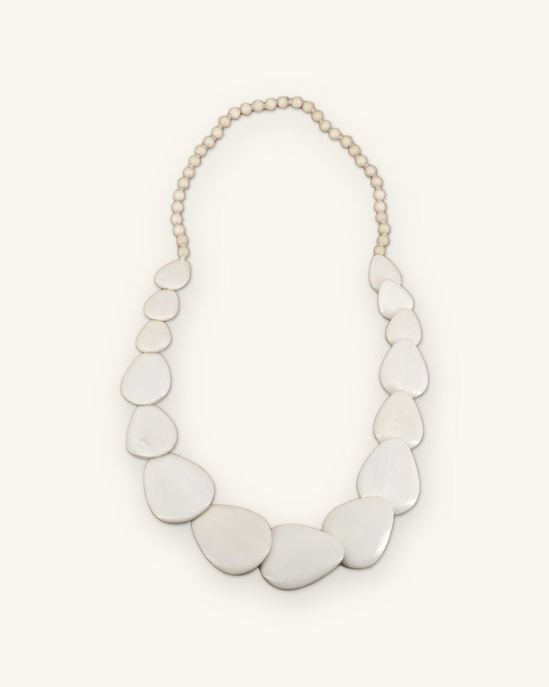 White guitar-pick shaped wood disc necklace on a round bead strand, laid flat, shown on a sand background