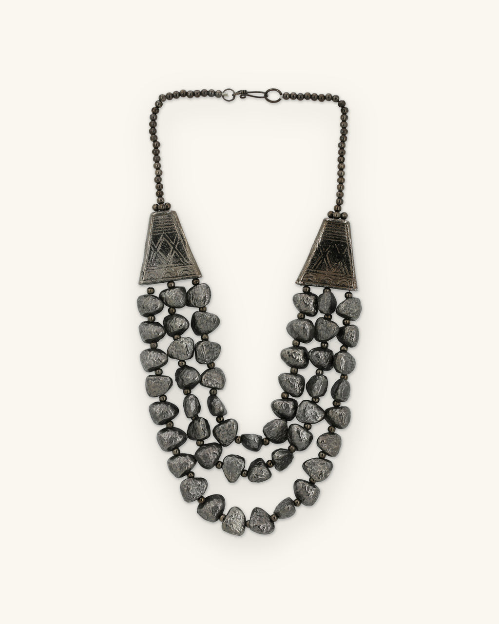 Gunmetal triple-strand necklace of textured pebble beads with etched cone ends, oxidized aluminum made in India, shown on a sand background