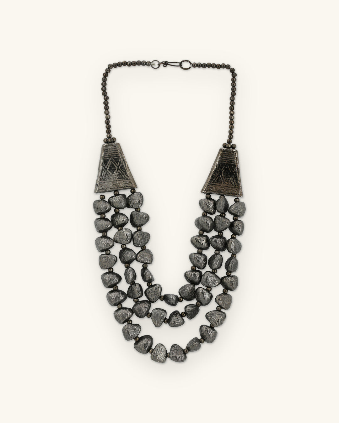 Gunmetal triple-strand necklace of textured pebble beads with etched cone ends, oxidized aluminum made in India, shown on a sand background