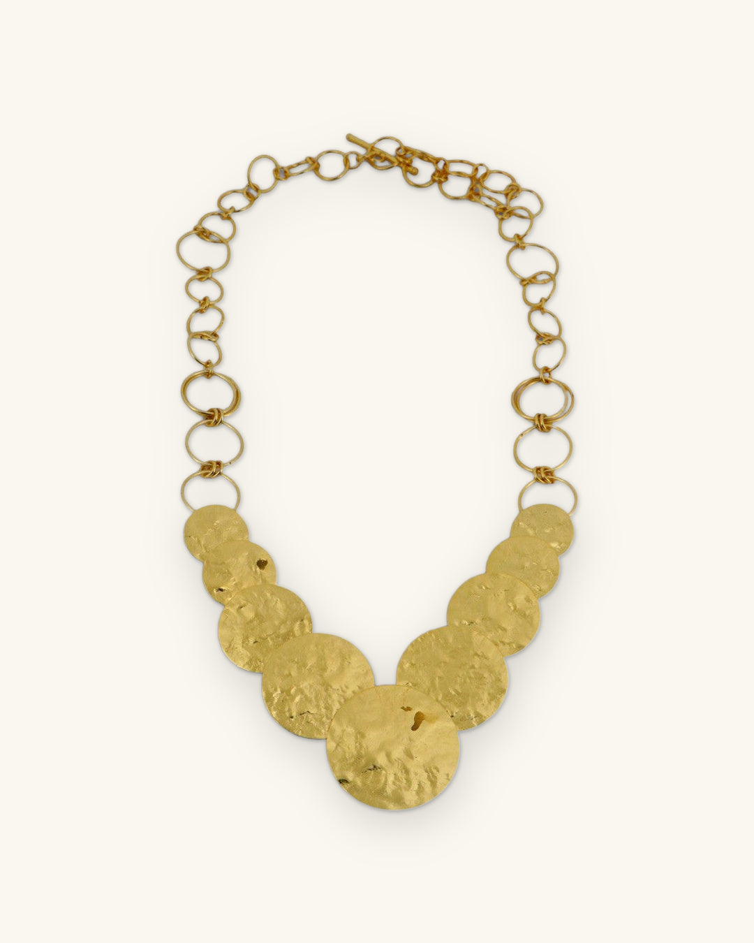Full hammered disc necklace laid flat, showing the link chain and toggle clasp, shown on a sand background