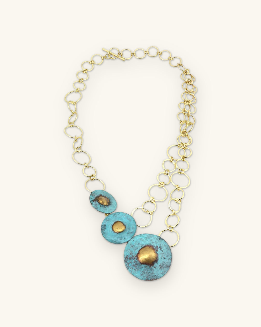 Full turquoise patina disc necklace laid flat, showing the brass link chains and toggle, shown on a sand background