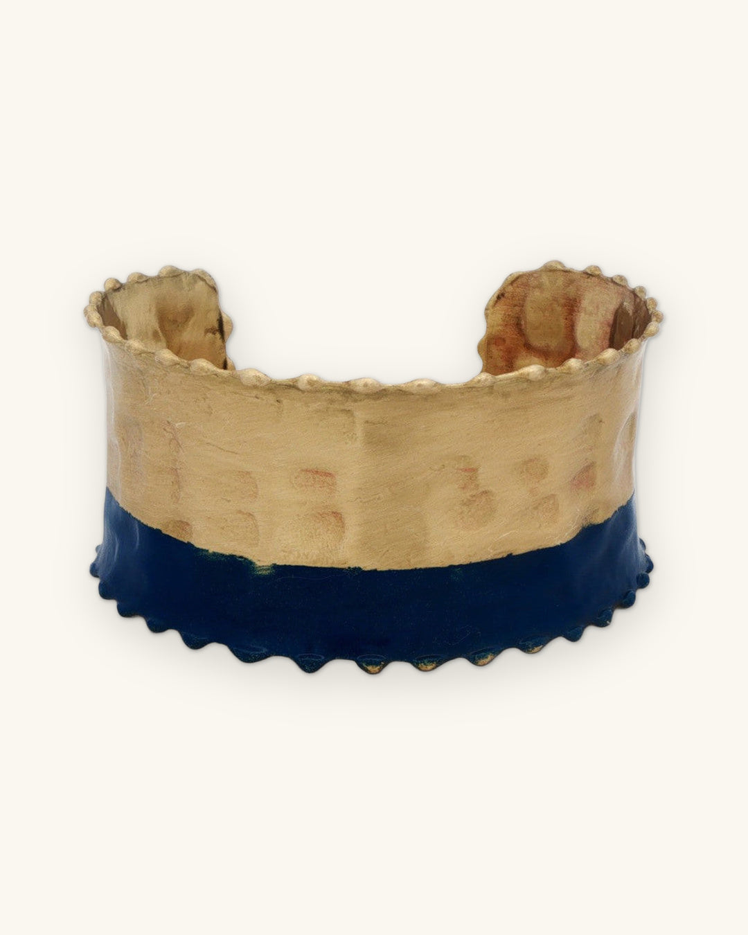 Front of the two-tone hammered cuff with antique gold top and indigo lower band, shown on a sand background