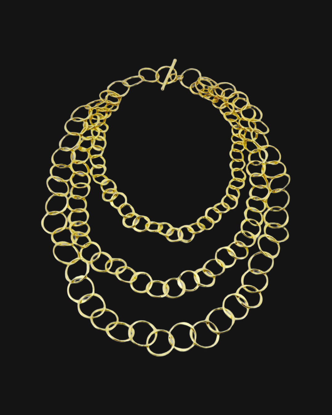 Graduated three-strand brass chain necklace laid flat with toggle clasp, shown on a black background