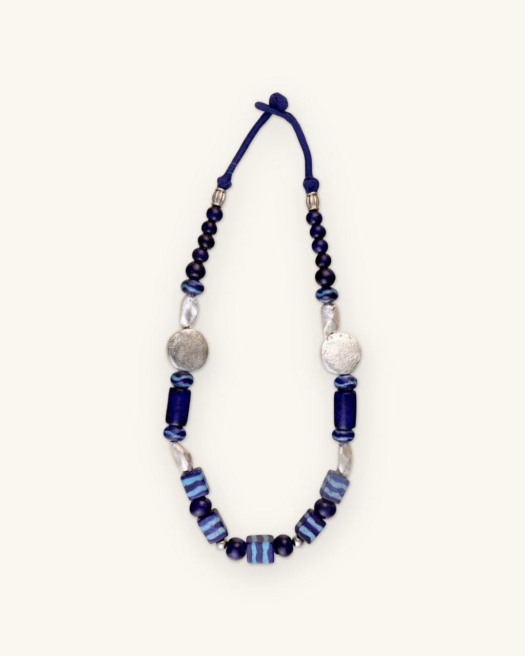Full indigo ceramic bead necklace laid flat with navy cord loop closure, shown on a sand background