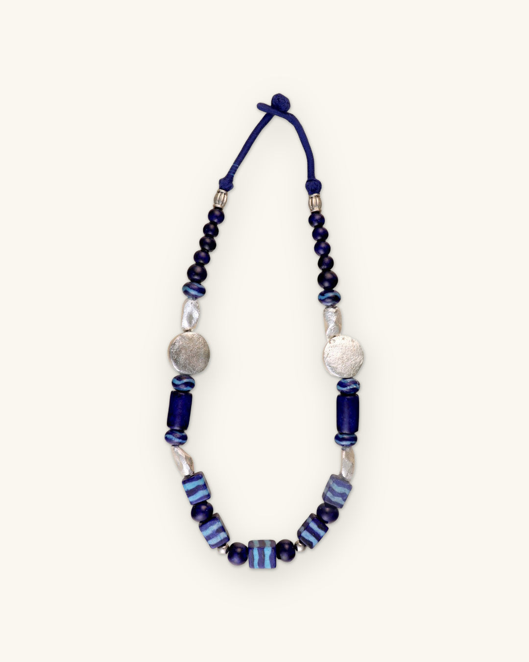 Full indigo ceramic bead necklace laid flat with navy cord loop closure, shown on a sand background