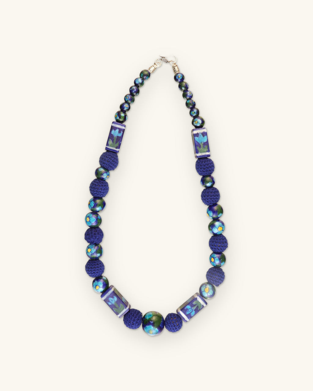 Full cobalt ceramic and crochet bead necklace laid flat with silver-tone clasp, shown on a sand background