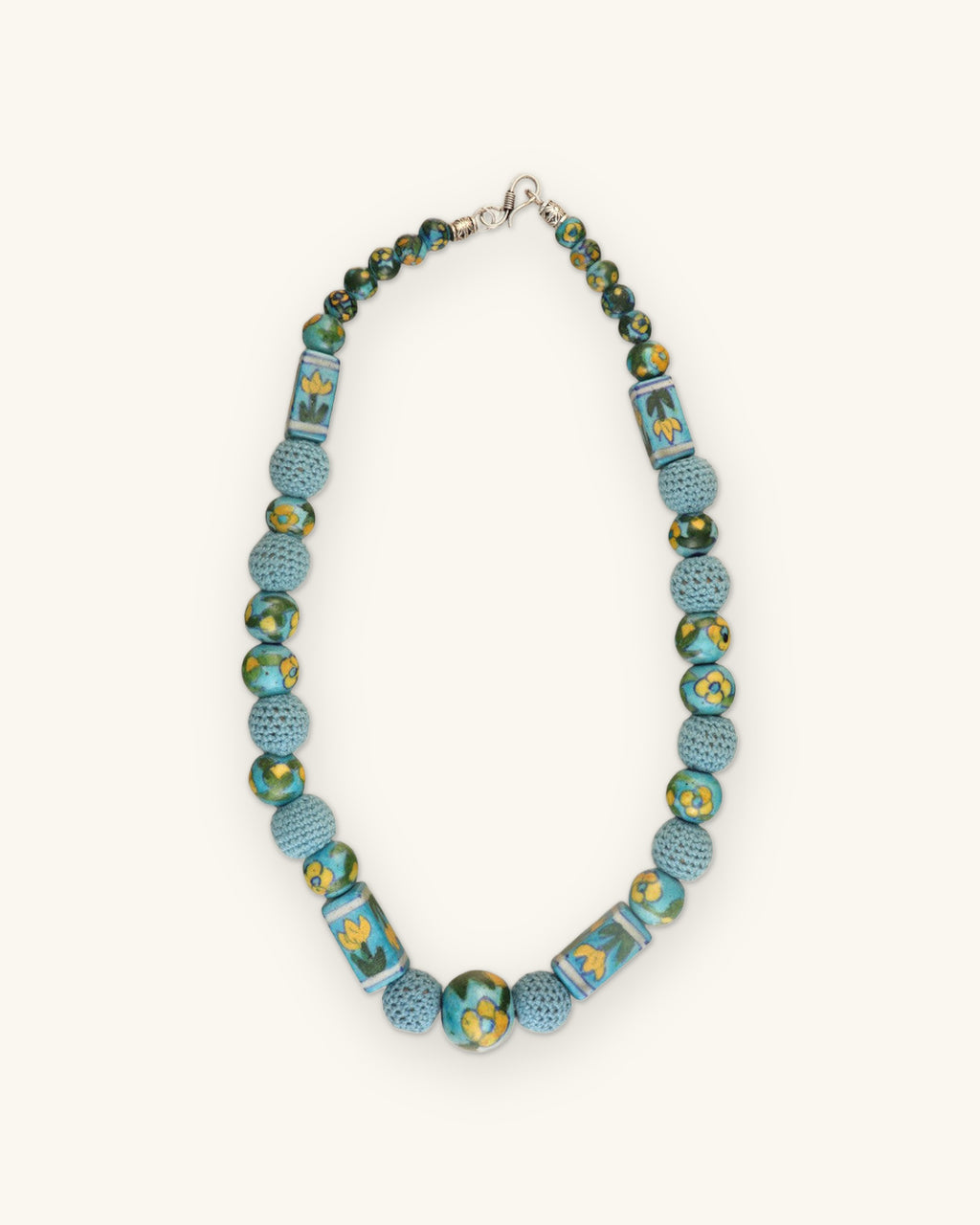 Full turquoise ceramic and crochet bead necklace laid flat with silver-tone clasp, shown on a sand background