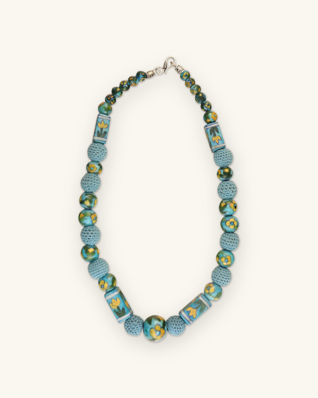 Full turquoise ceramic and crochet bead necklace laid flat with silver-tone clasp, shown on a sand background