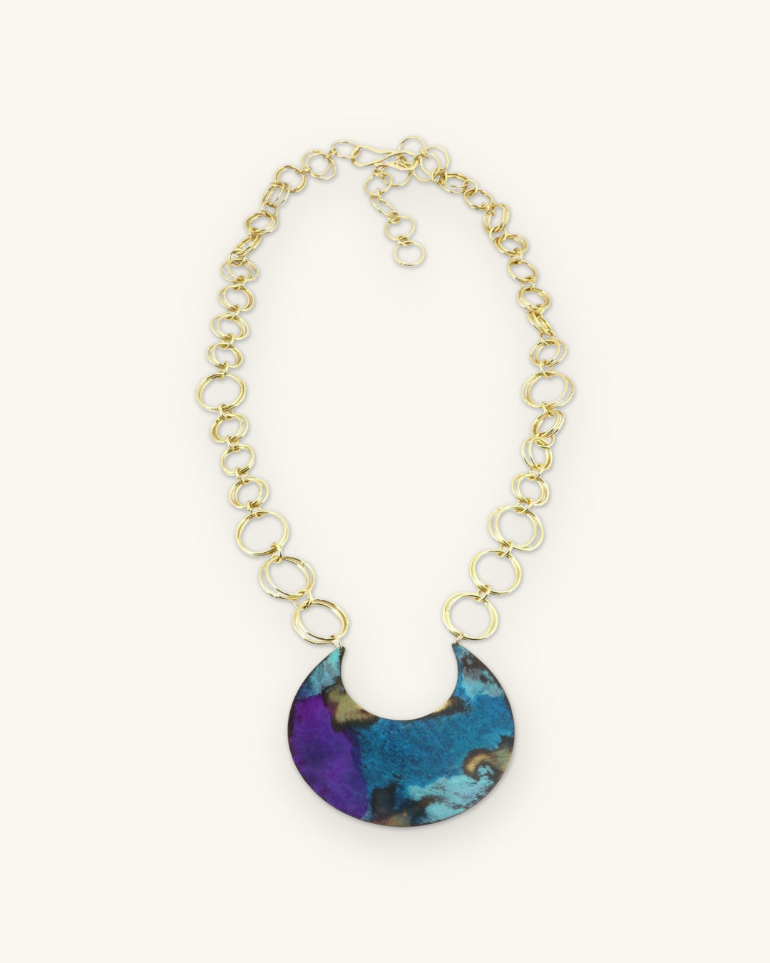 Full crescent pendant necklace laid flat with brass ring-link chain and hook clasp, shown on a sand background
