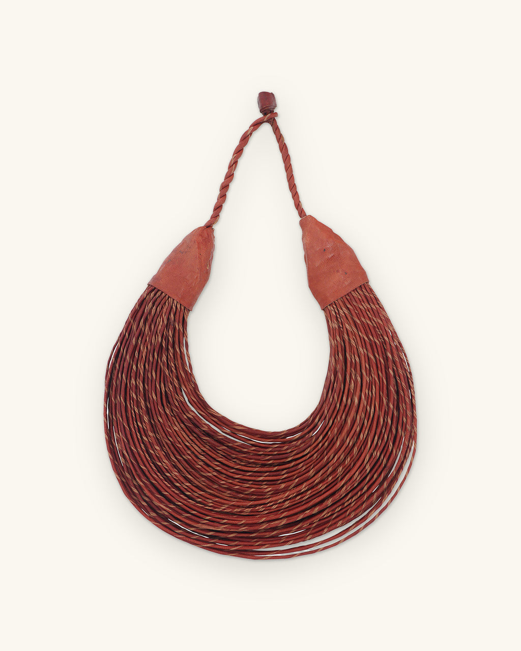 Crescent of many twisted leather cords in deep rust with leather end caps and braided loop, shown on a sand background