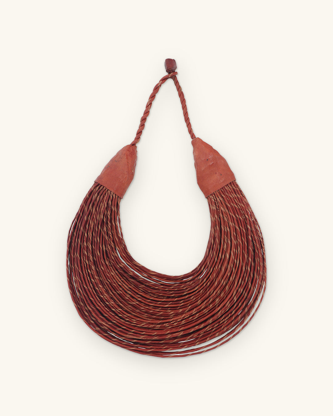 Crescent of many twisted leather cords in deep rust with leather end caps and braided loop, shown on a sand background