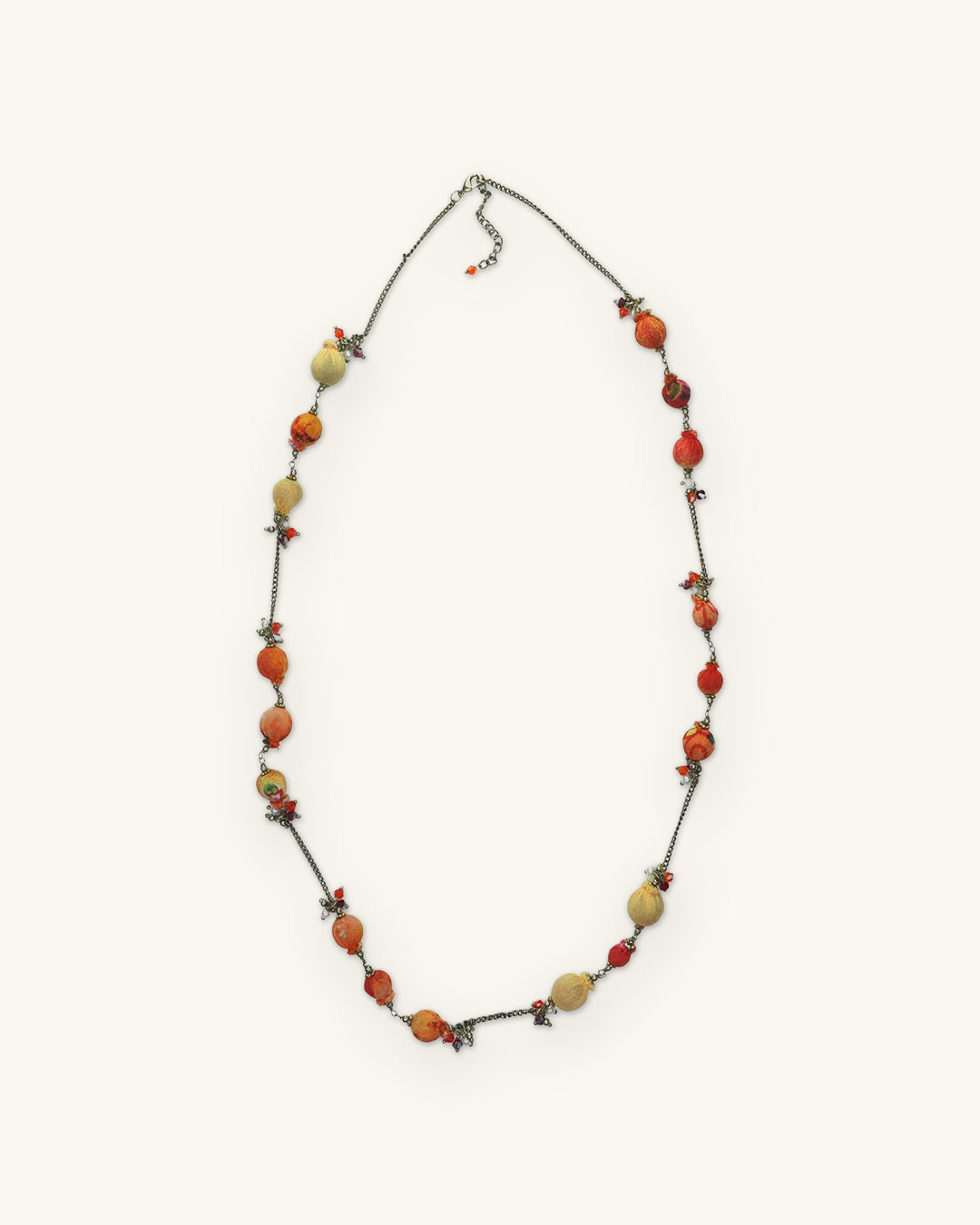 Long fabric-wrapped bead necklace in Orange with tan and red beads on brass chain, shown on a sand background