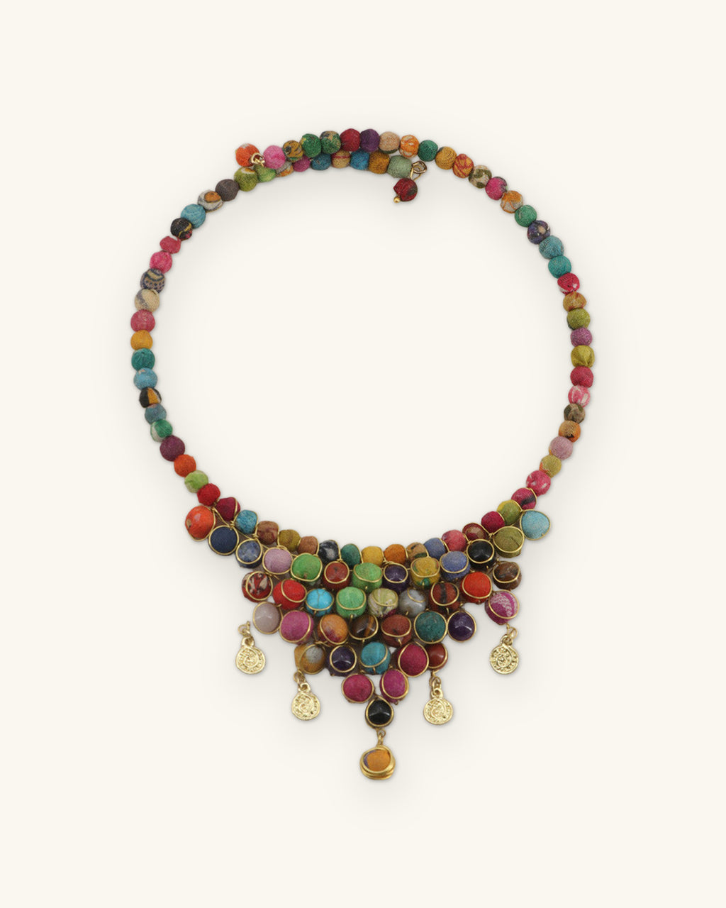 Full round multicolor textile bead choker laid flat, cluster bib and gold-tone coin drops at the front, shown on a sand background