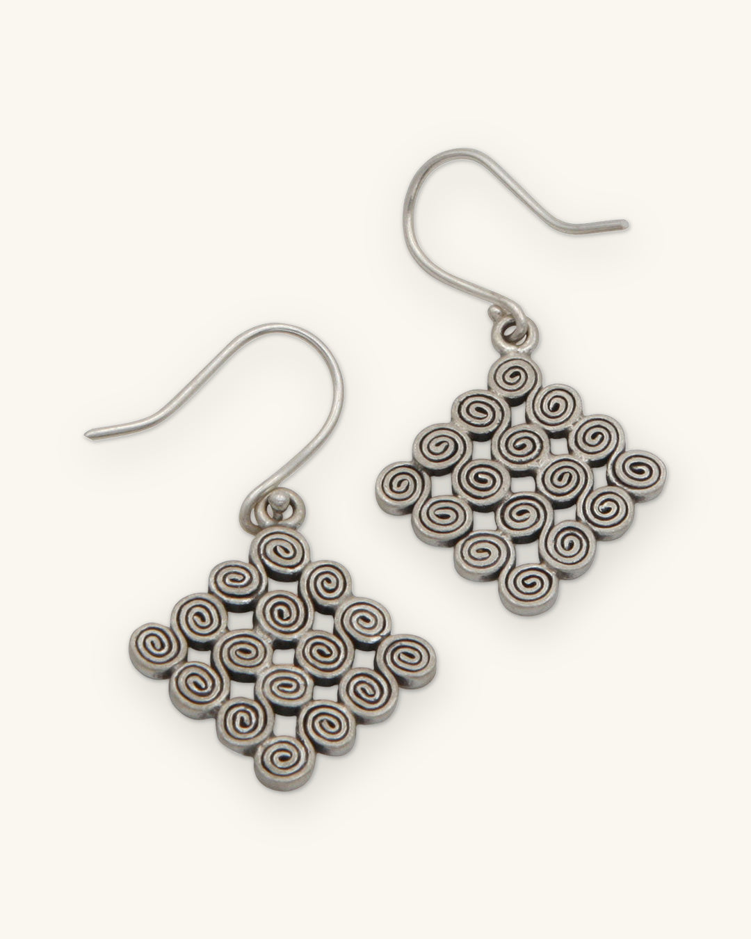 Pair of silver spiral diamond drop earrings on fish-hook ear wires, shown on a sand background