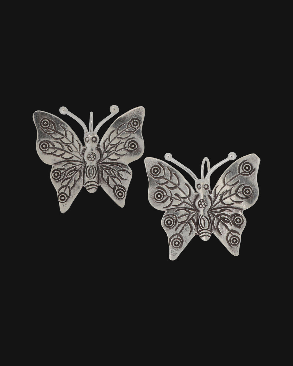 Pair of silver butterfly earrings with stamped swirl and leaf wing patterns, shown on a black background