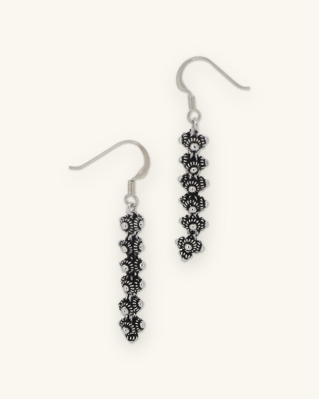 Stacked floret drop earrings in oxidized hill tribe silver on sterling fish-hook ear wires, handmade in Laos, shown on a sand background