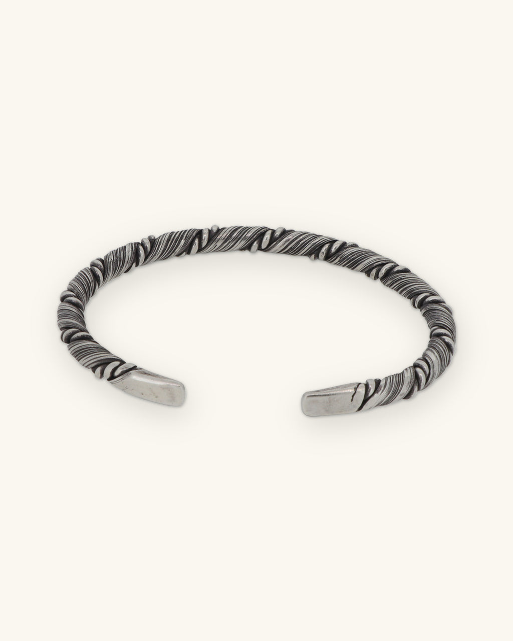 Sterling silver twist cuff turned to show its open adjustable ends, shown on a sand background