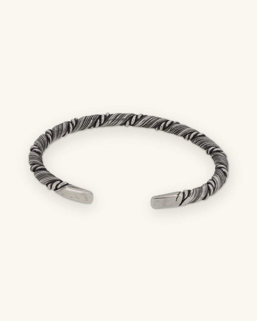Sterling silver twist cuff turned to show its open adjustable ends, shown on a sand background