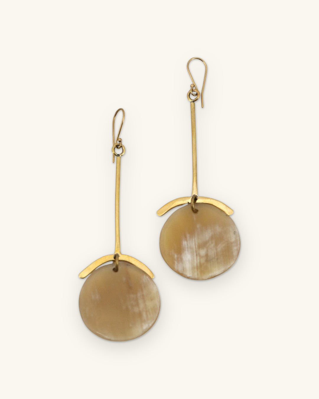 Long hammered brass bar earrings with honey-toned horn discs and curved brass caps, handmade in Kenya, shown on a sand background
