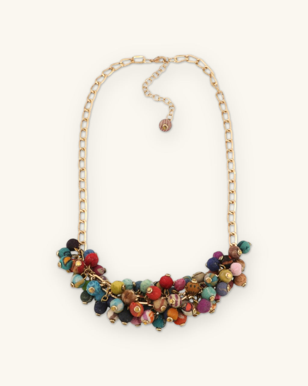 Crescent of red, teal, gold and purple fabric beads on a long brass chain with extender and charm, shown on a sand background