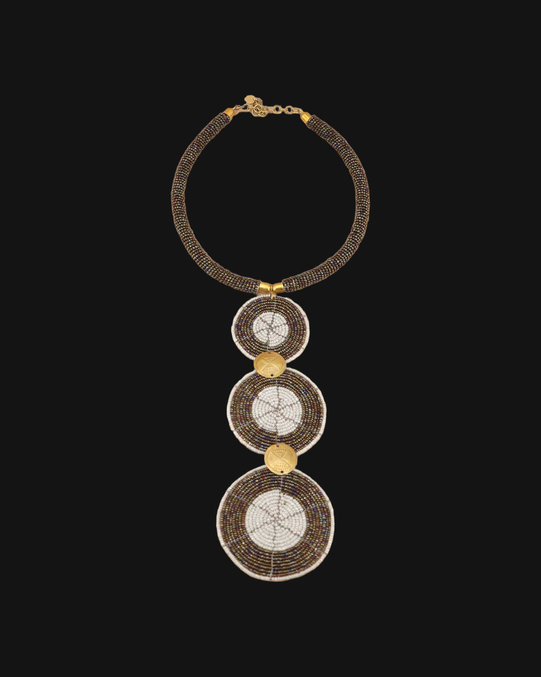 Brown glass bead collar necklace laid flat with three white-centered bead discs linked by brass coins, shown on a black background