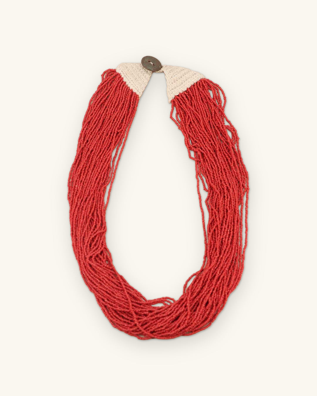 Multi-strand scarlet glass seed bead necklace with cream cotton crochet shoulders and button closure, made in Nepal, shown on a sand background