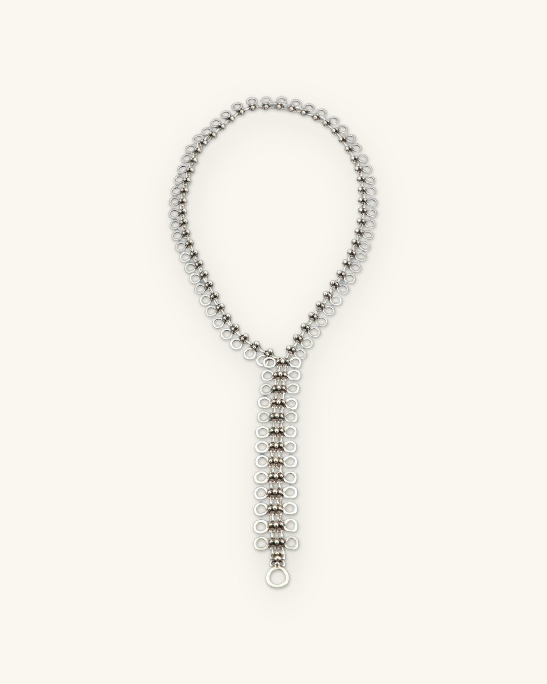 Full length of the polished silver-tone cutout disc lariat necklace laid flat in a Y shape, shown on a sand background