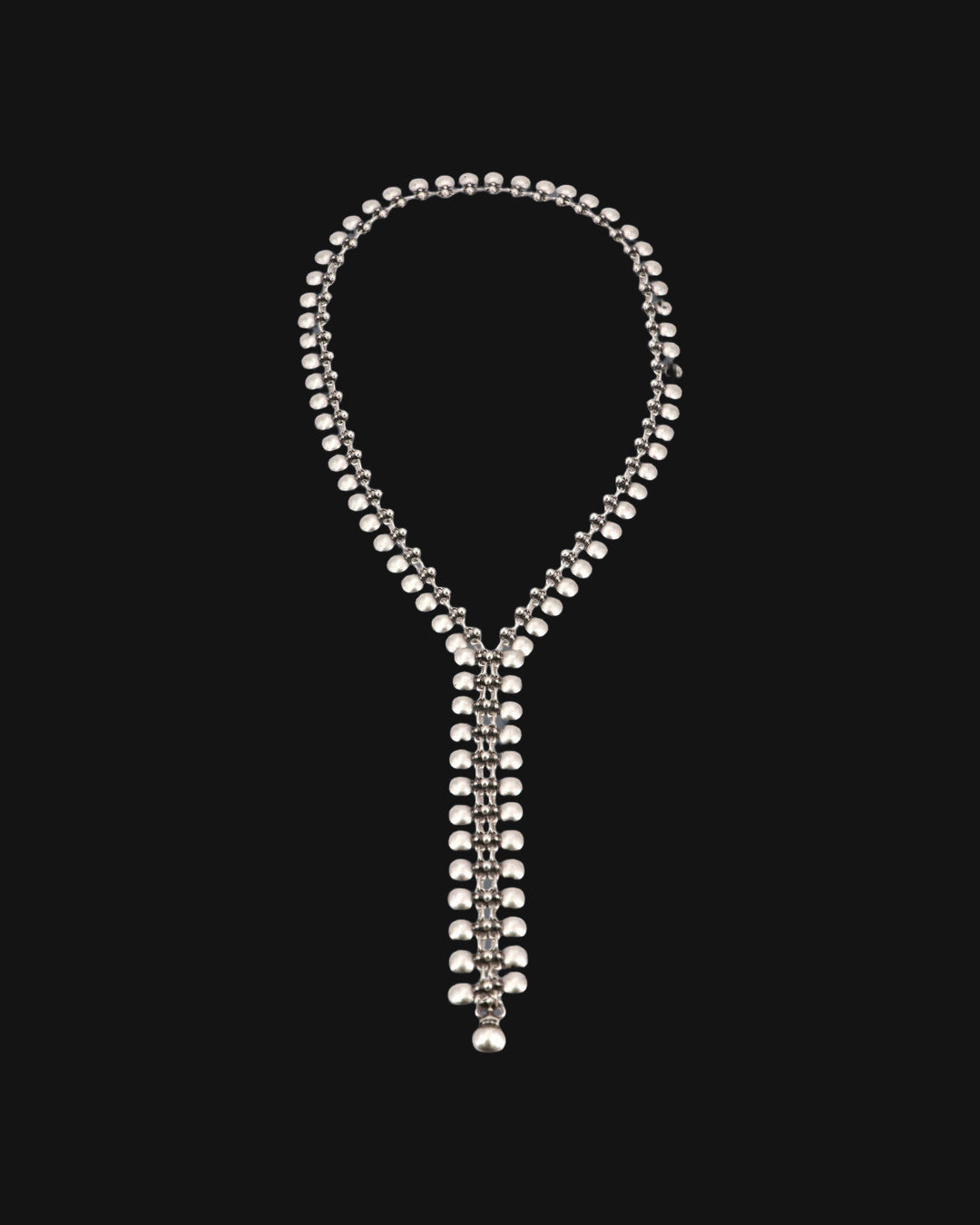Full loop of the silver-tone bead-link lariat necklace laid flat with its narrow woven drop, shown on a black background