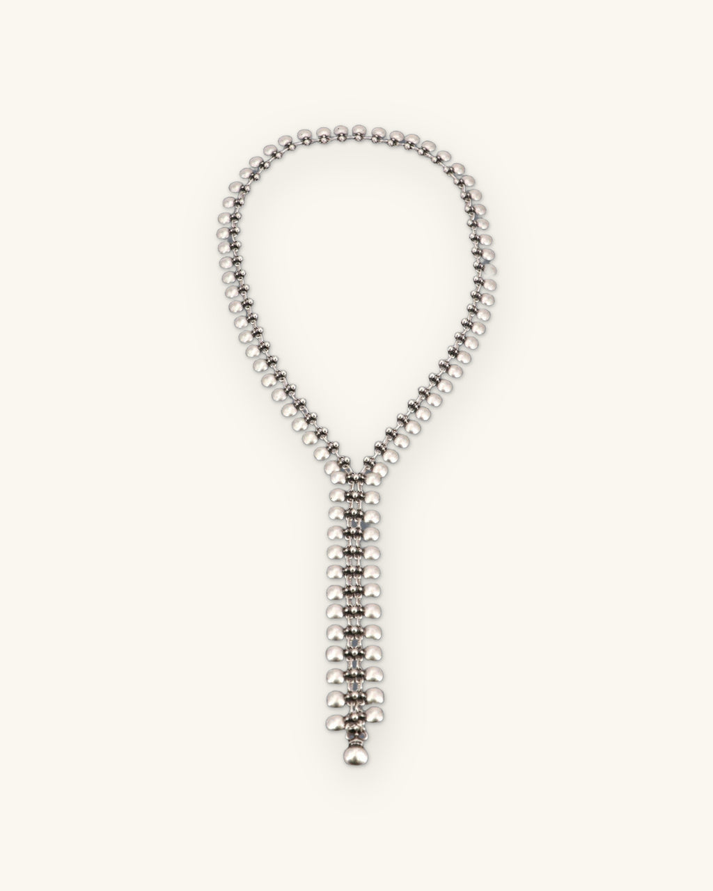 Full loop of the silver-tone bead-link lariat necklace laid flat with its narrow woven drop, shown on a sand background