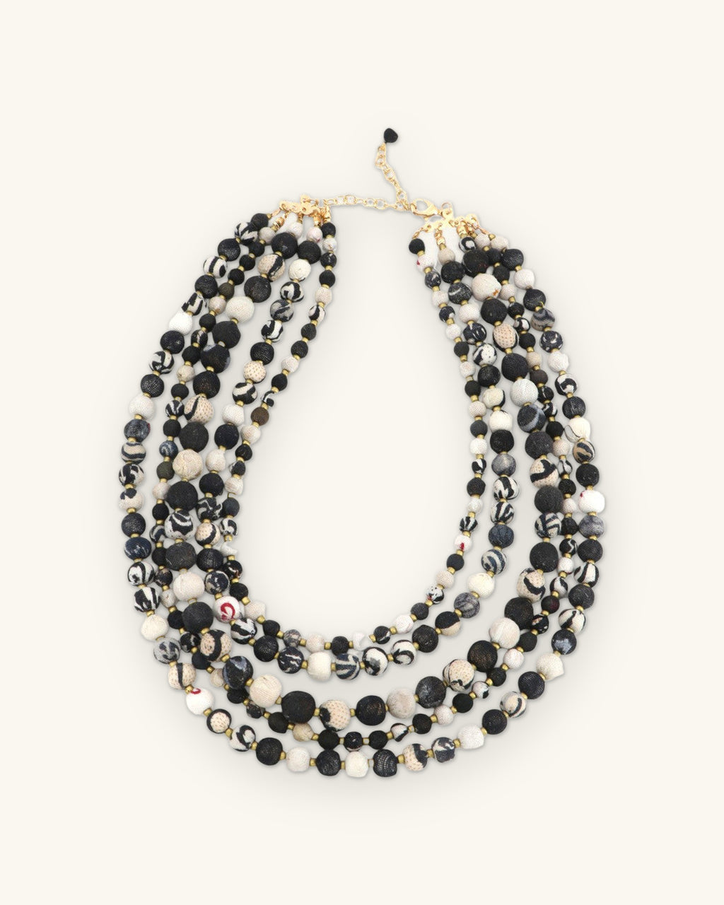 Layered black and ivory bead necklace laid flat with its chain closure and black bead drop, shown on a sand background