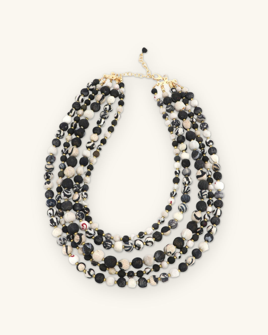 Layered black and ivory bead necklace laid flat with its chain closure and black bead drop, shown on a sand background