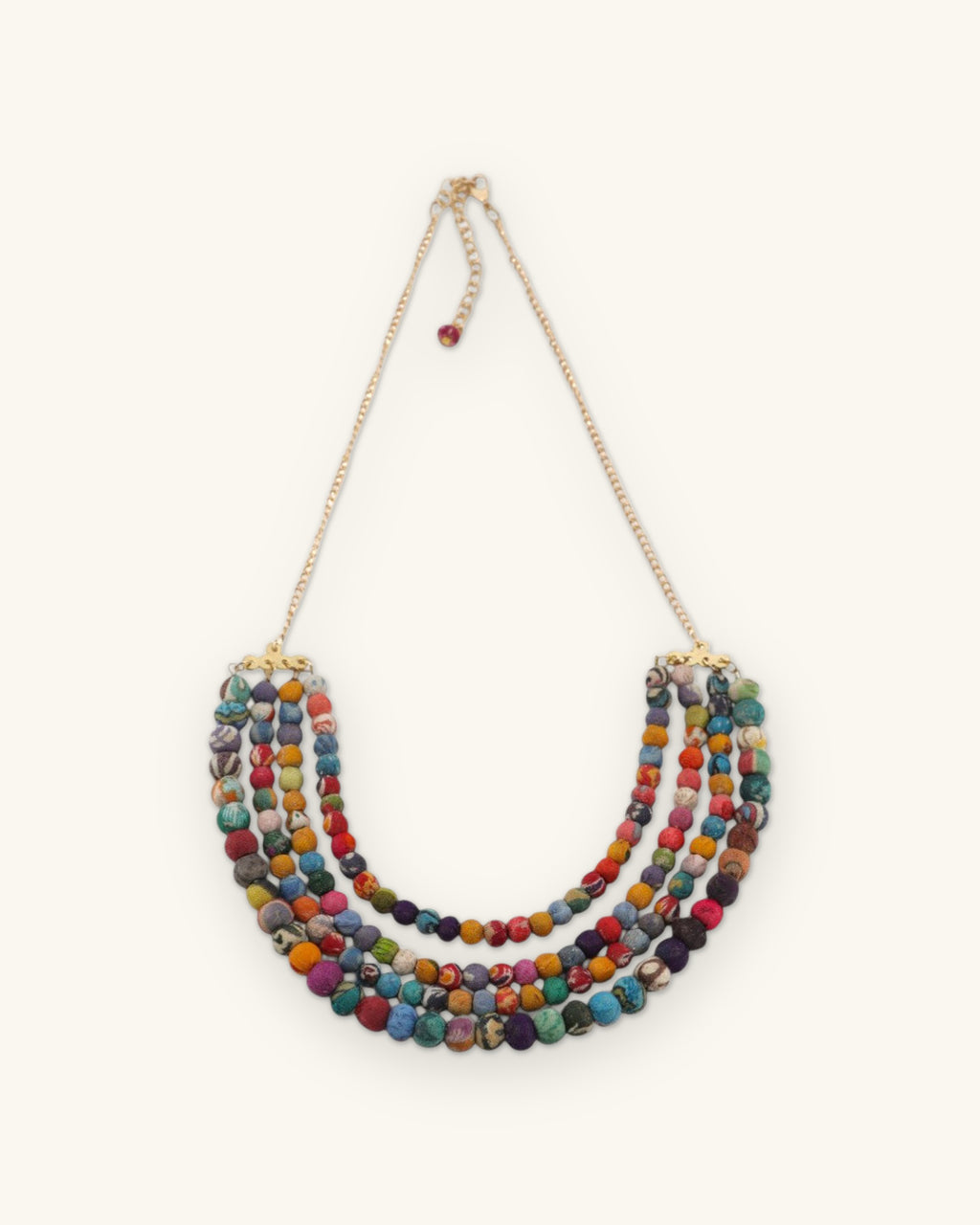 Full length of the Kantha fabric bead necklace with gold-tone chain, clasp and bead drop, shown on a sand background