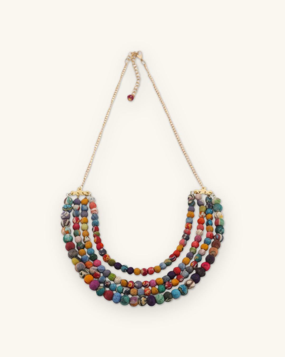 Full length of the Kantha fabric bead necklace with gold-tone chain, clasp and bead drop, shown on a sand background