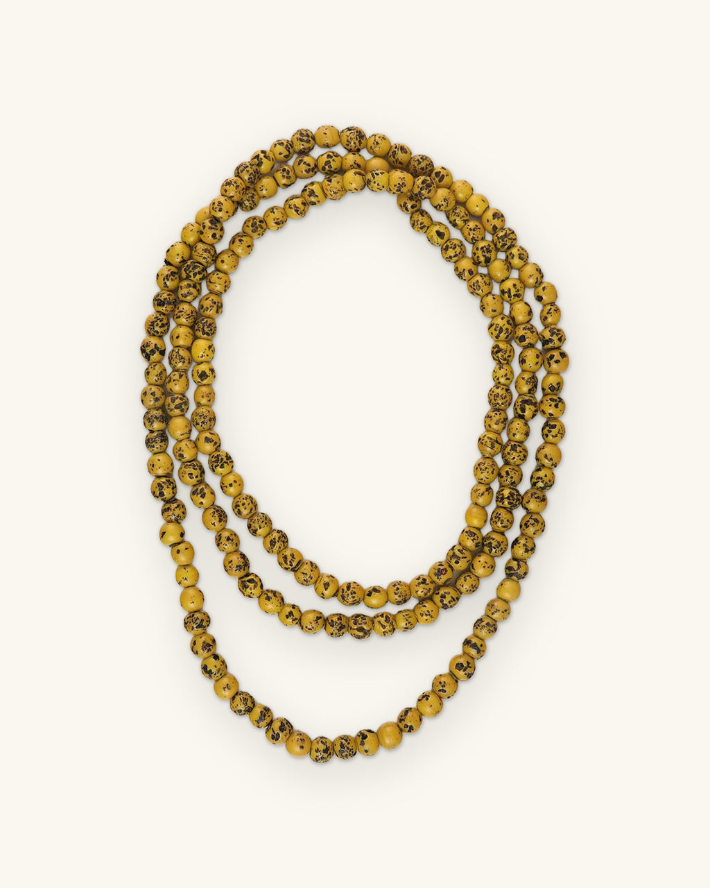 Endless glass bead necklace in Yellow with dark antique speckling, looped in three rows, shown on a sand background