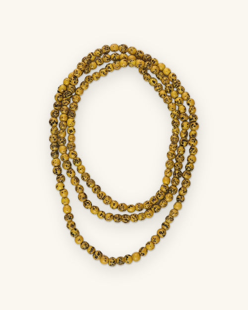 Endless glass bead necklace in Yellow with dark antique speckling, looped in three rows, shown on a sand background