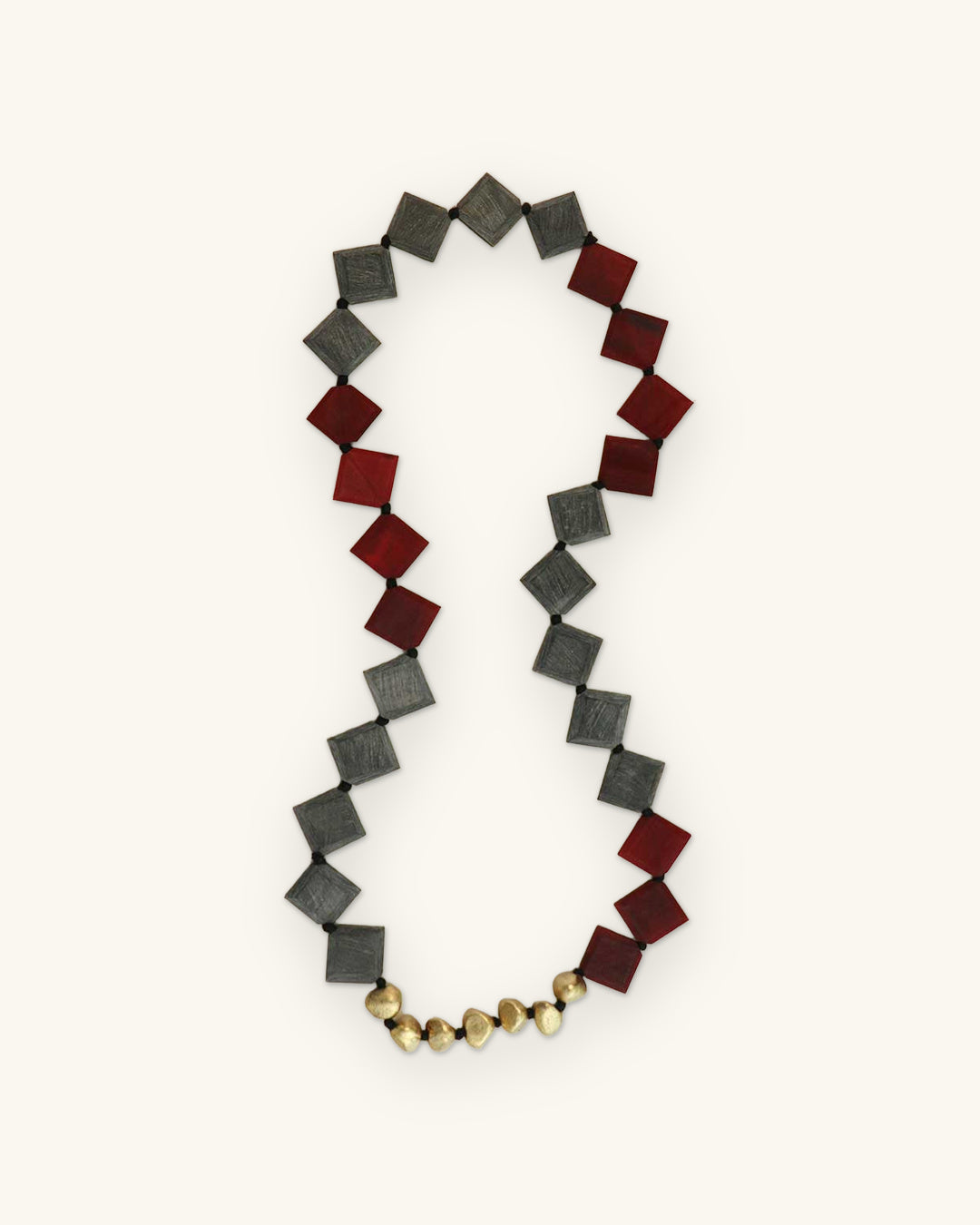 Red and gray diamond-set horn bead necklace laid in a figure-eight shape with round brass beads at the base, shown on a sand background