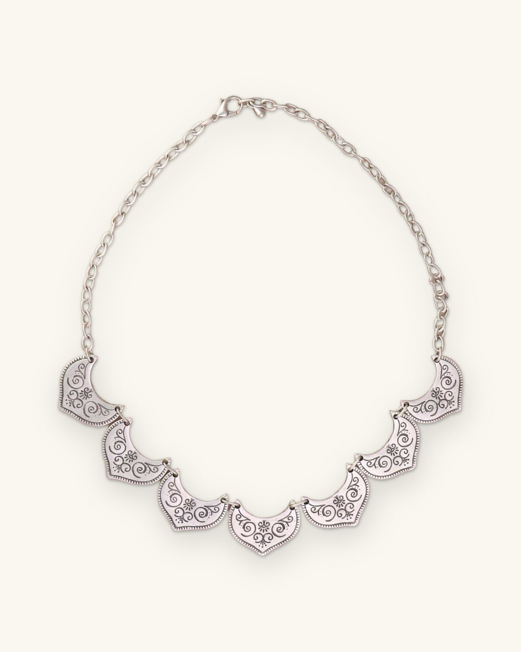 Silver-tone fan-plate bib necklace laid flat with its link chain and lobster clasp, shown on a sand background