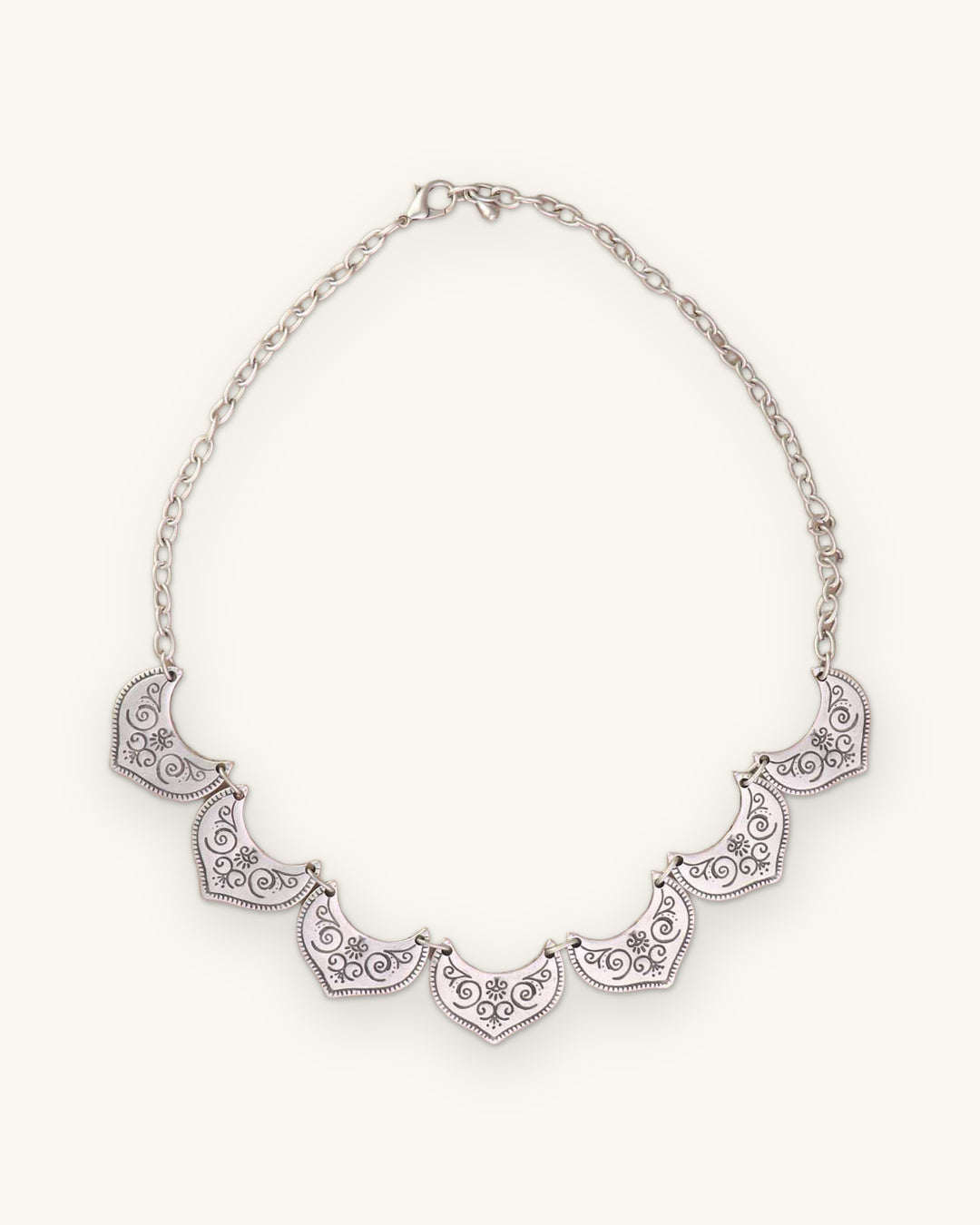 Silver-tone fan-plate bib necklace laid flat with its link chain and lobster clasp, shown on a sand background