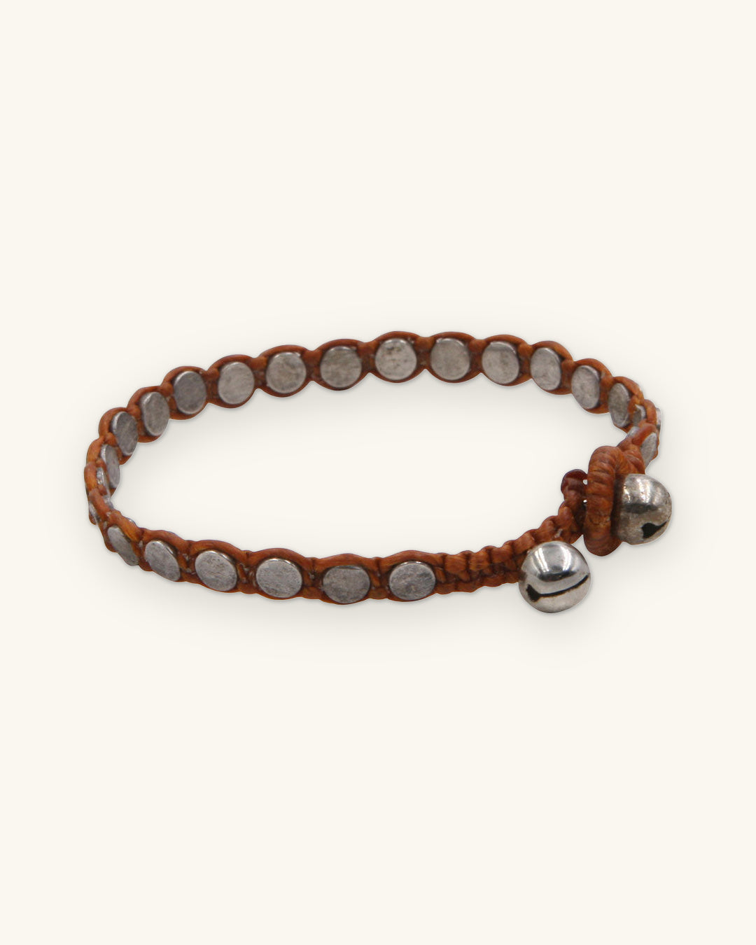 Woven disk bracelet in Sienna with metal disk beads and two silver-tone bell closures, shown on a sand background