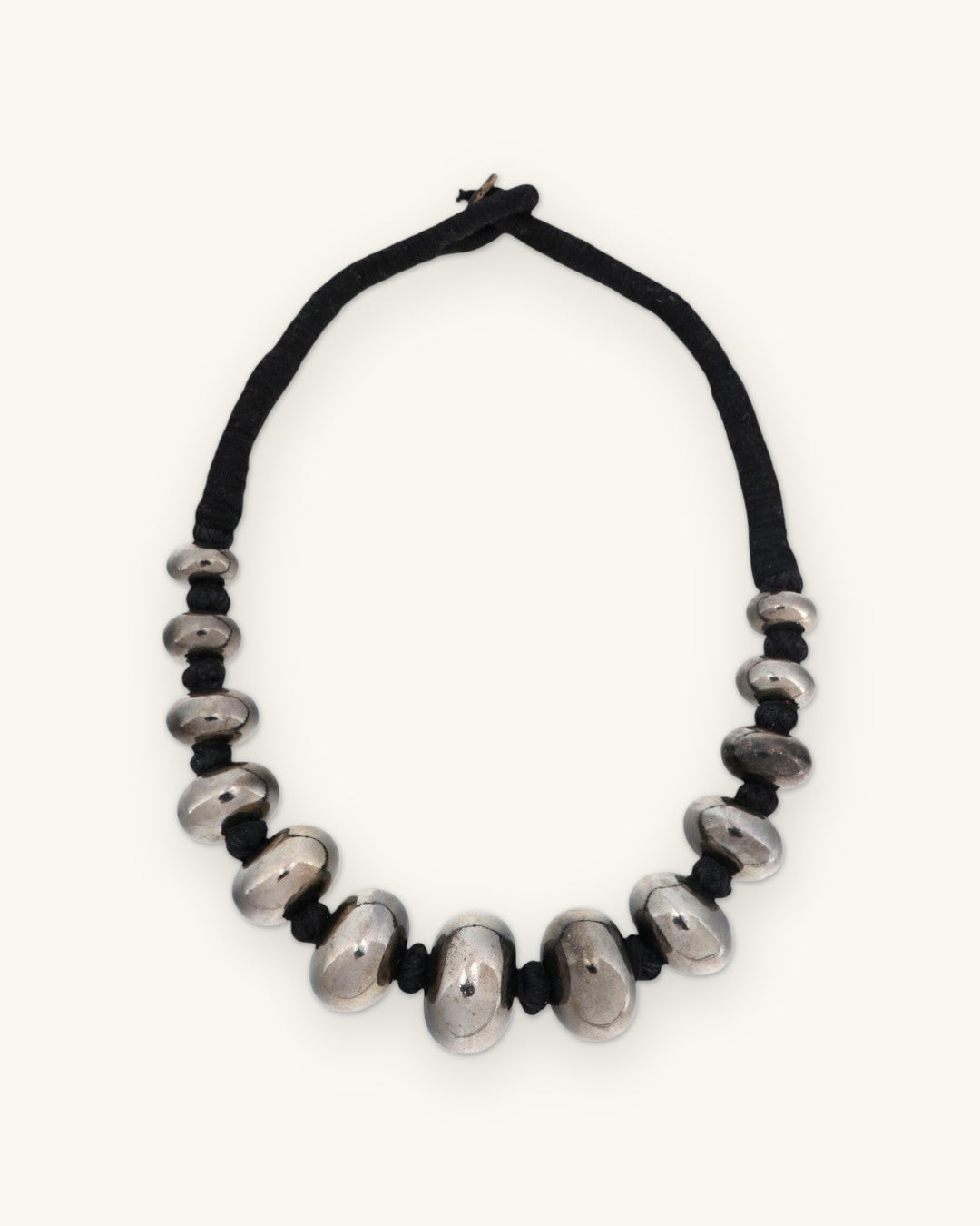 Full view of the graduated gunmetal bead necklace with wrapped black cord and loop closure, shown on a sand background