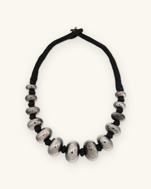 Full view of the graduated gunmetal bead necklace with wrapped black cord and loop closure, shown on a sand background