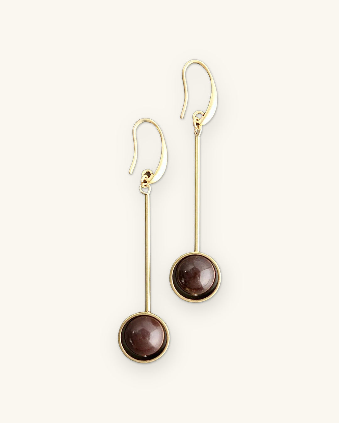 Bar-and-sphere drop earrings with brown agate cabochons bezel-set in 18k gold-plated brass, made in the USA, shown on a sand background