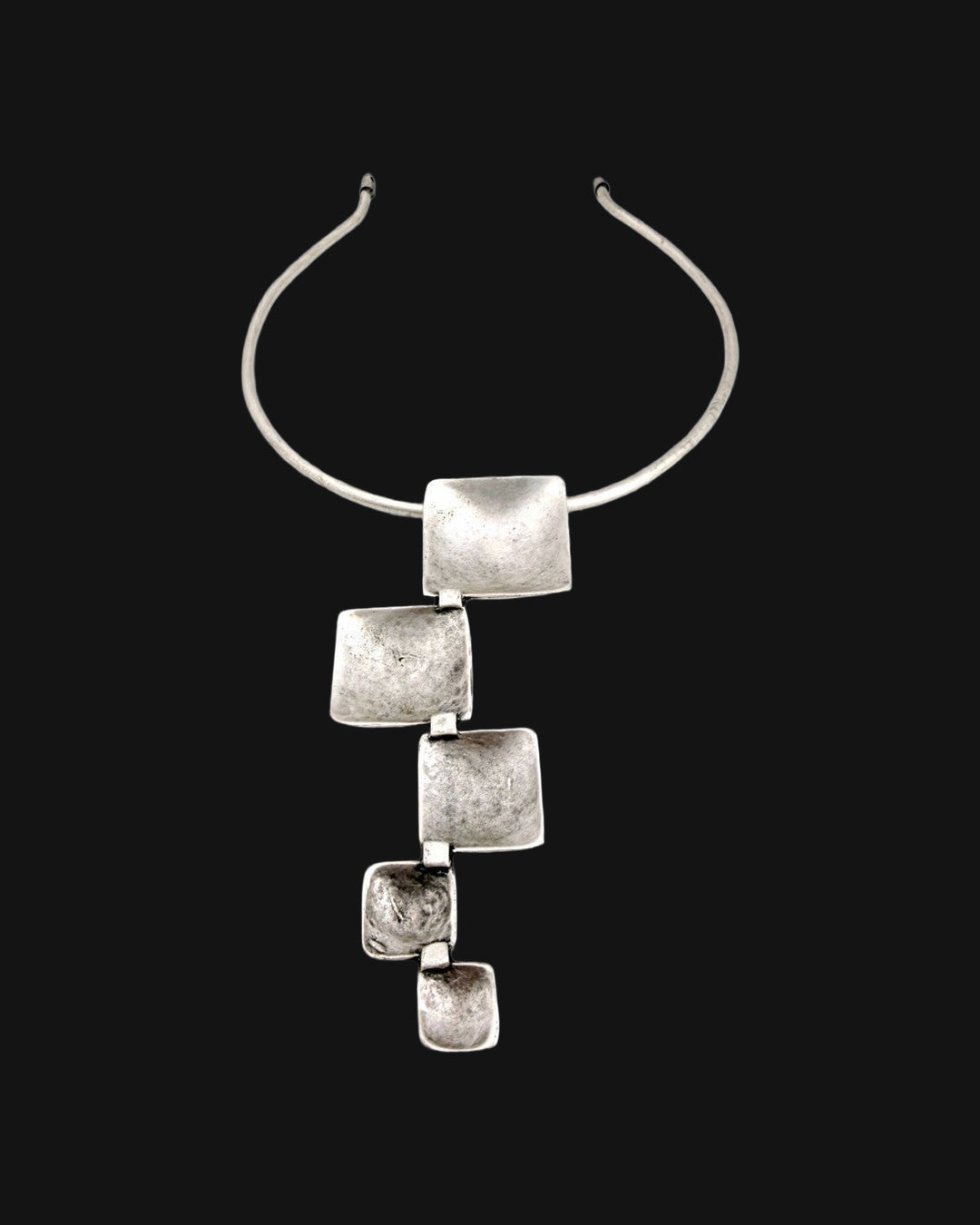 Close-up of the textured, cupped silver-tone squares linked below the rigid collar, shown on a black background